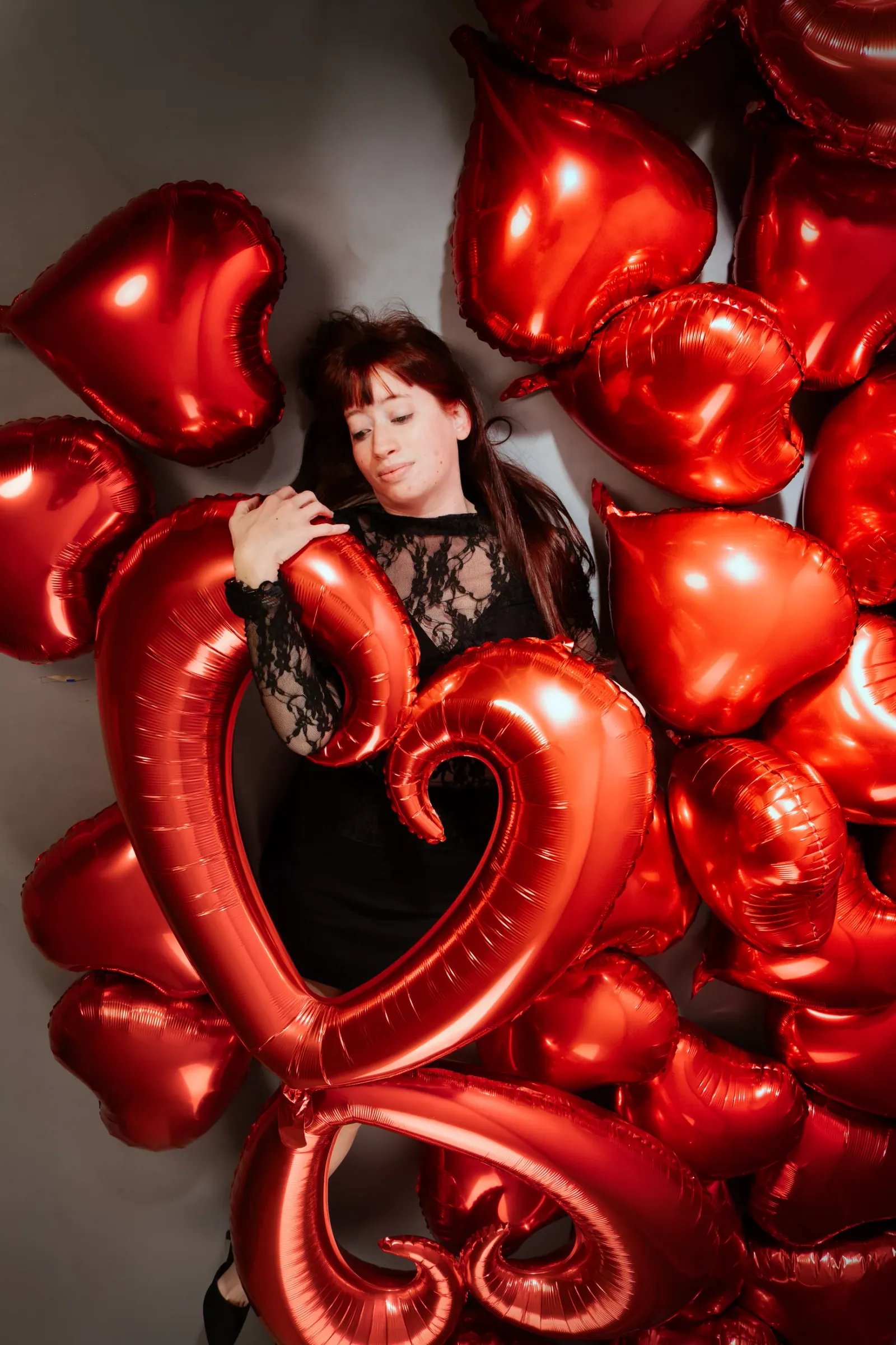 Black lace boudoir portrait among rich red heart balloons