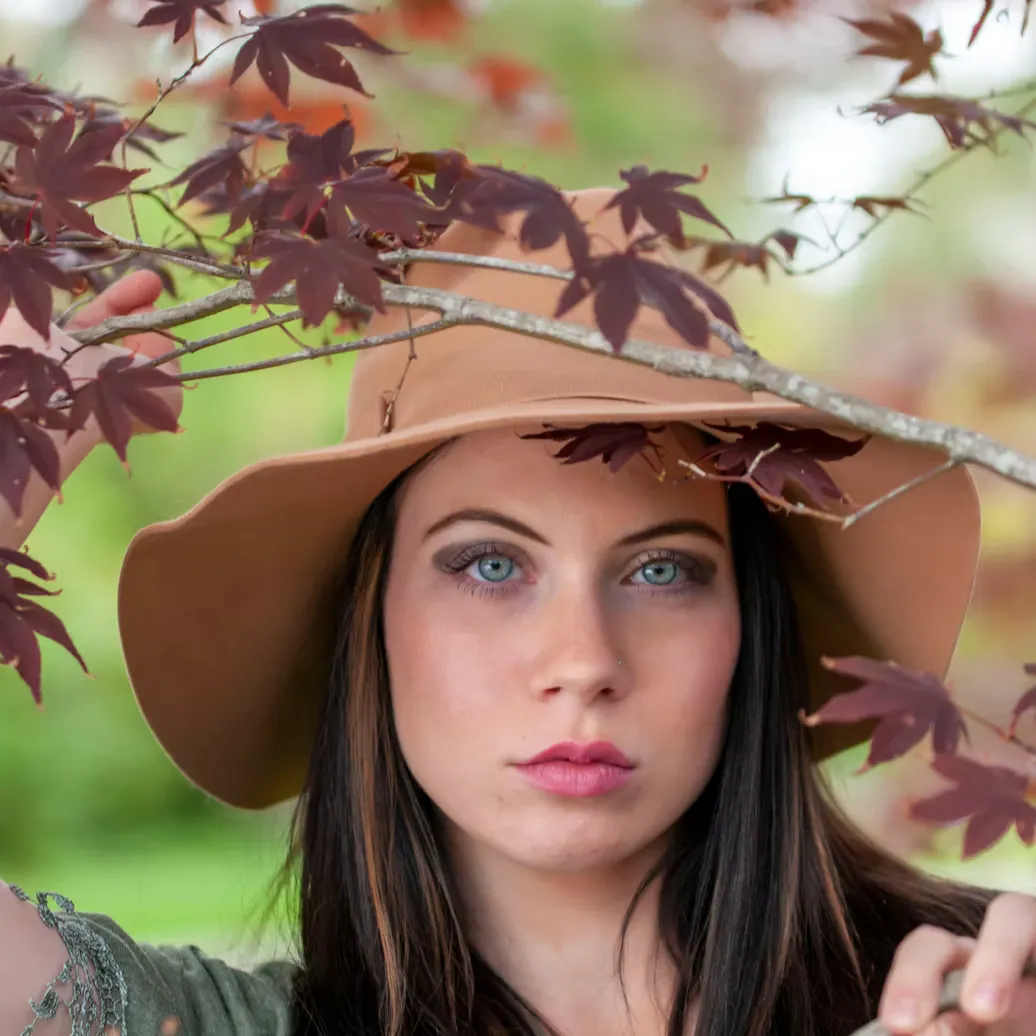 Fashion portrait beneath autumn leaves in a wide-brimmed hat