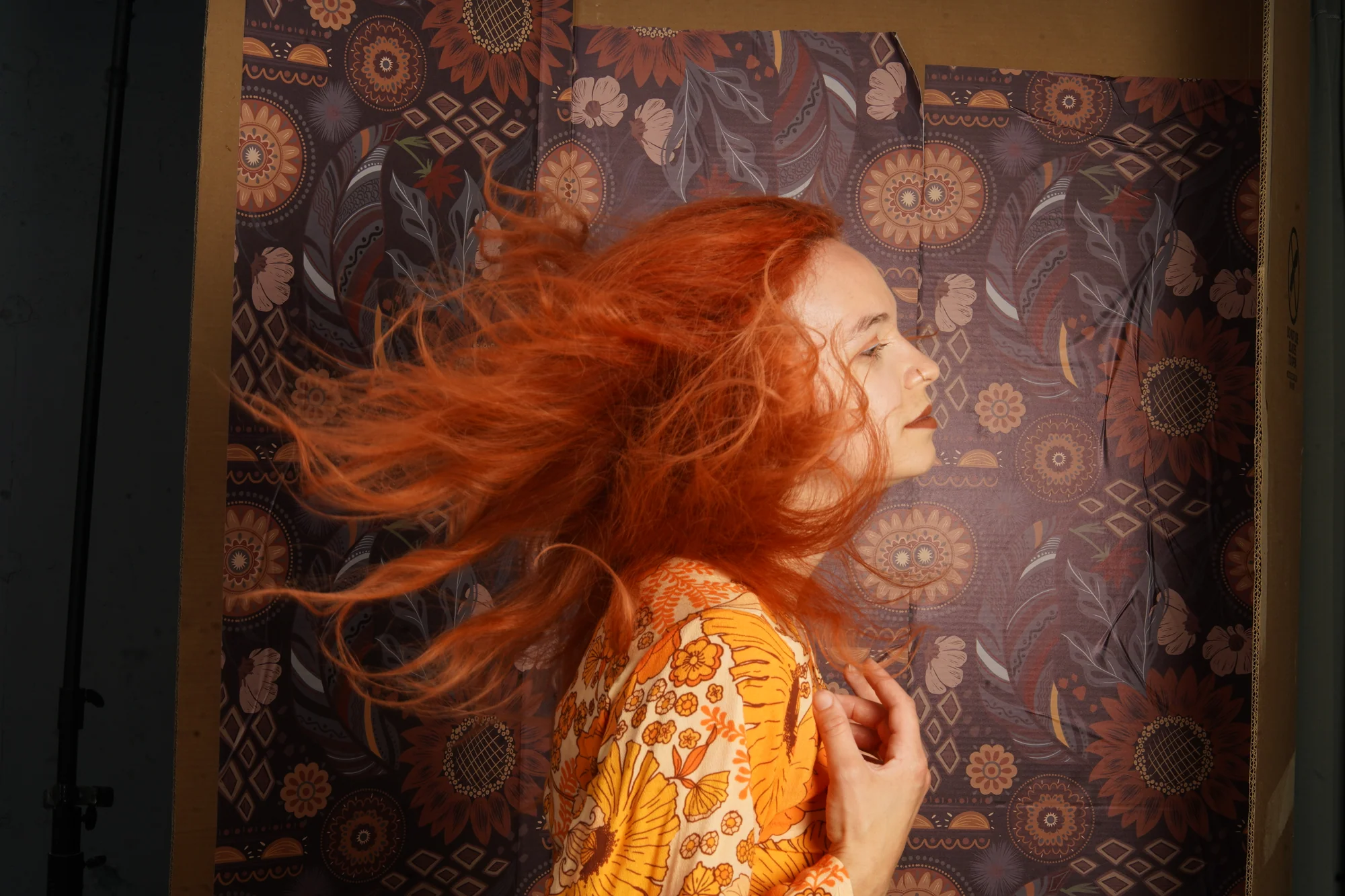 Wind-swept fashion portrait in warm orange against a patterned backdrop