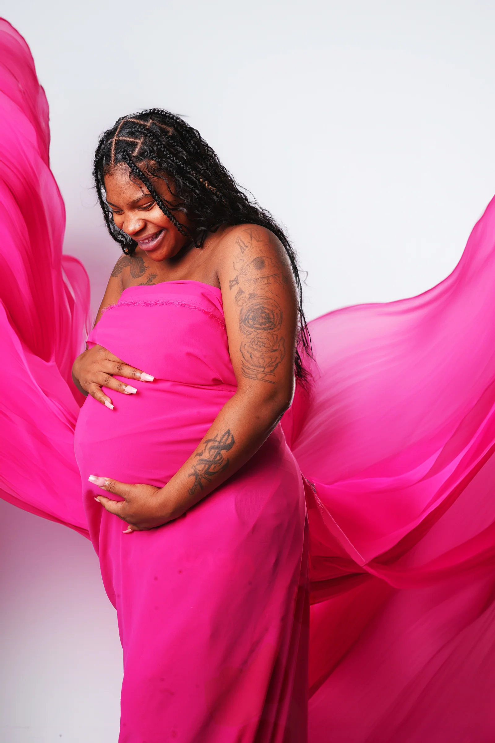 Expectant mother wrapped in flowing magenta fabric for a joyful studio portrait